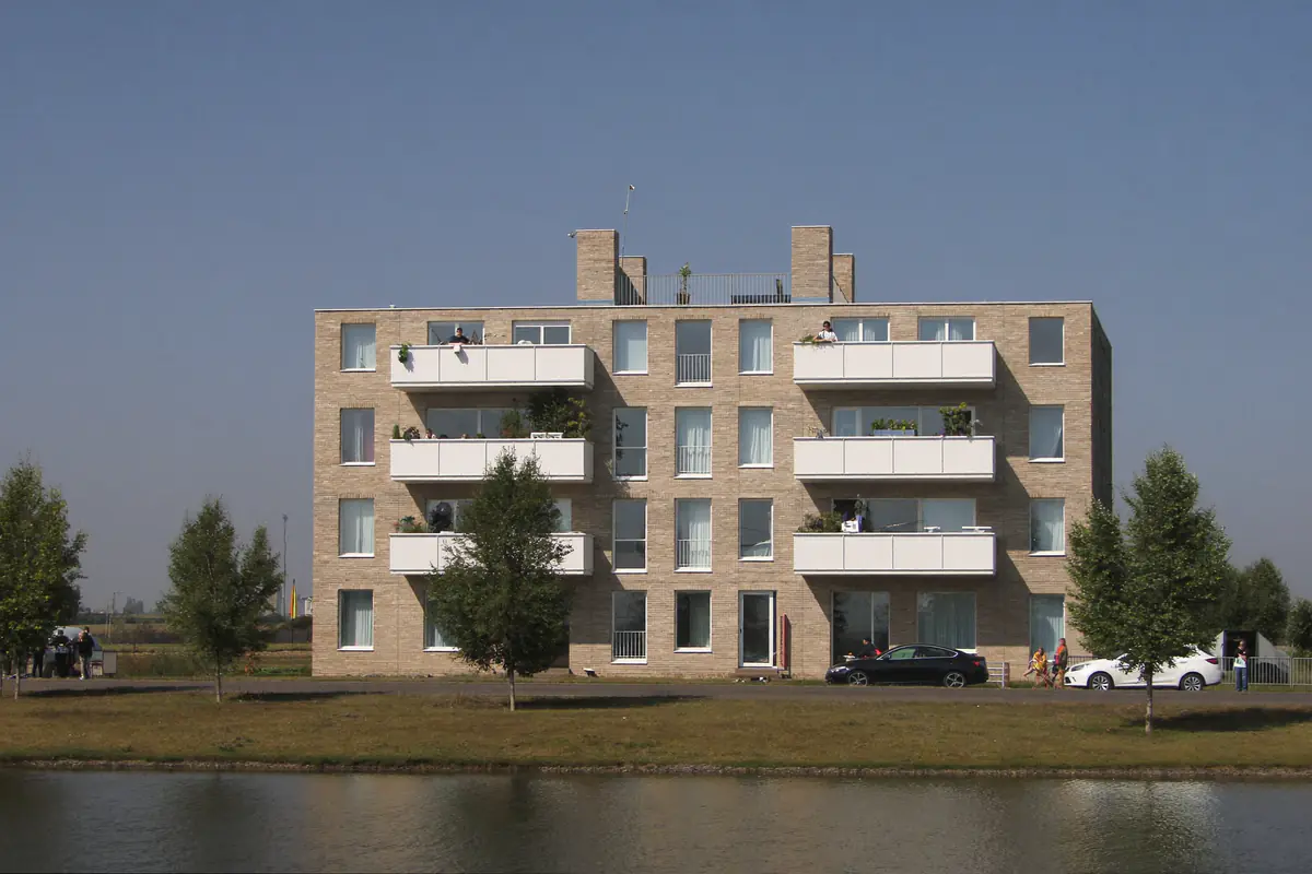 Modern appartementengebouw van lichte baksteen met witte balkons aan het water in een vlakke nieuwbouwwijk